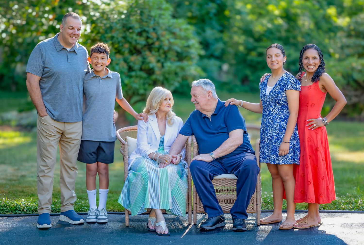 Family of six posing outdoors, smiling together in a lush green setting, dressed in casual and semi-formal attire.