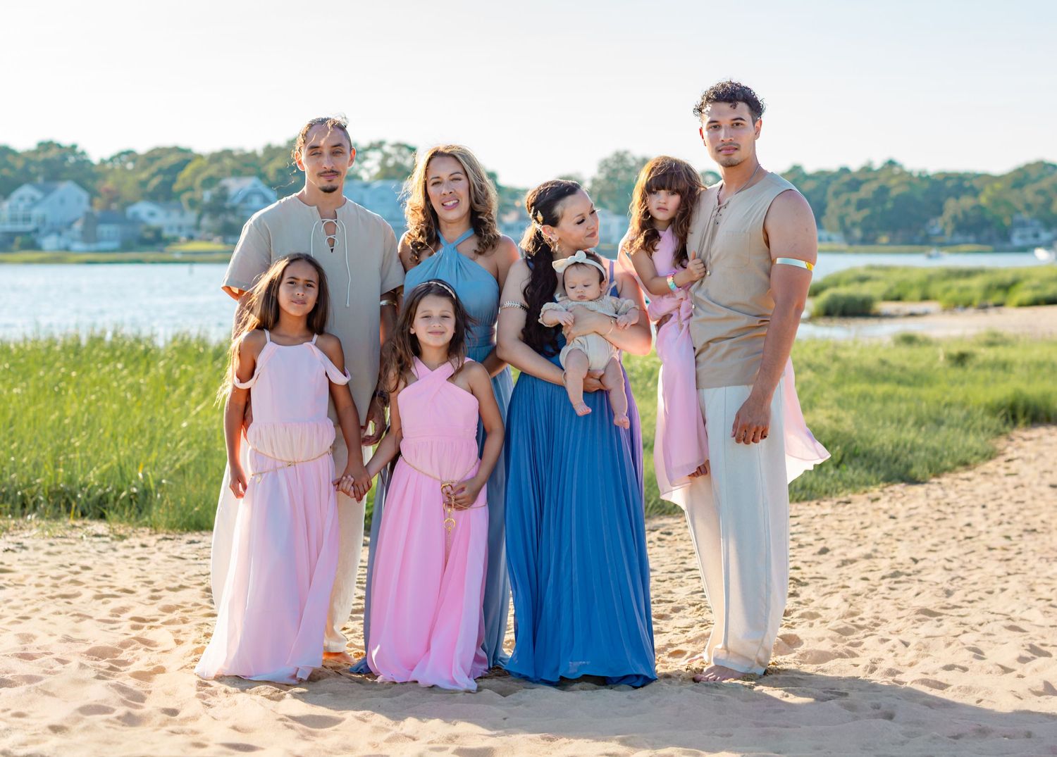 Family of seven posing together on a sandy beach in coordinated pink and blue outfits on a sunny day.