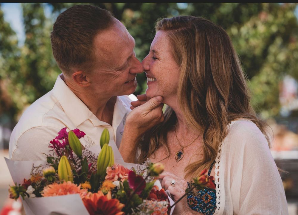 Couple sharing a romantic moment with colorful bouquet of flowers outdoors on a sunny day.