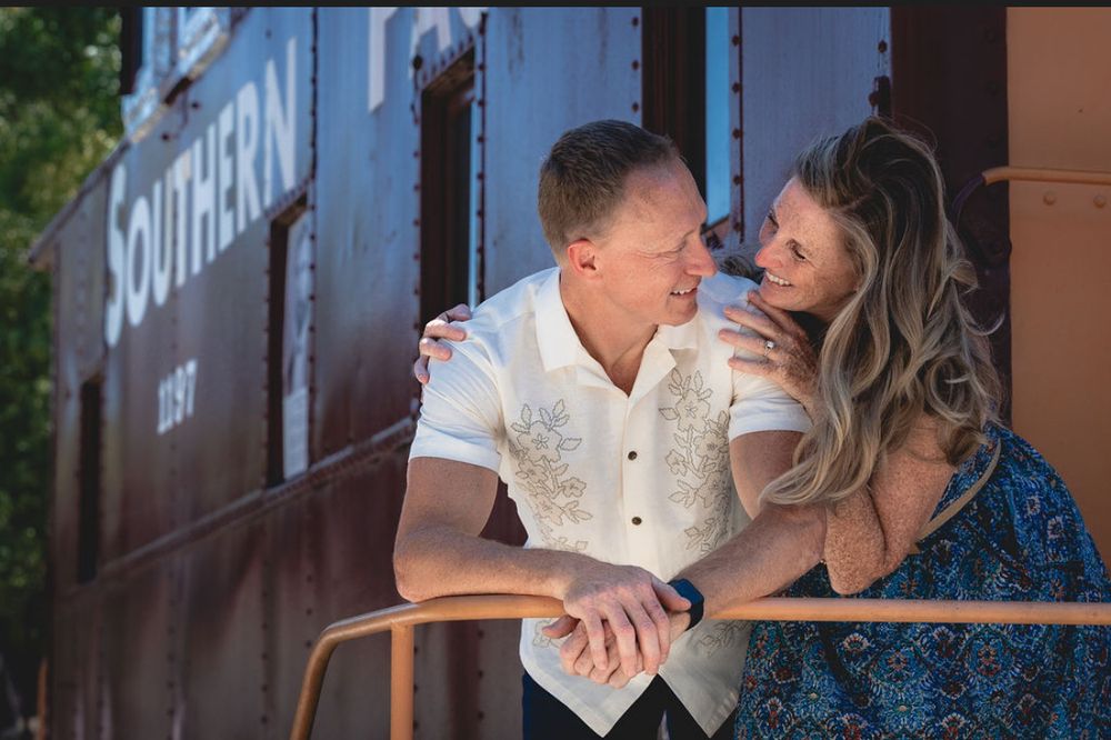Couple smiling and embracing near a vintage Southern railway train car during an outdoor engagement photo session.