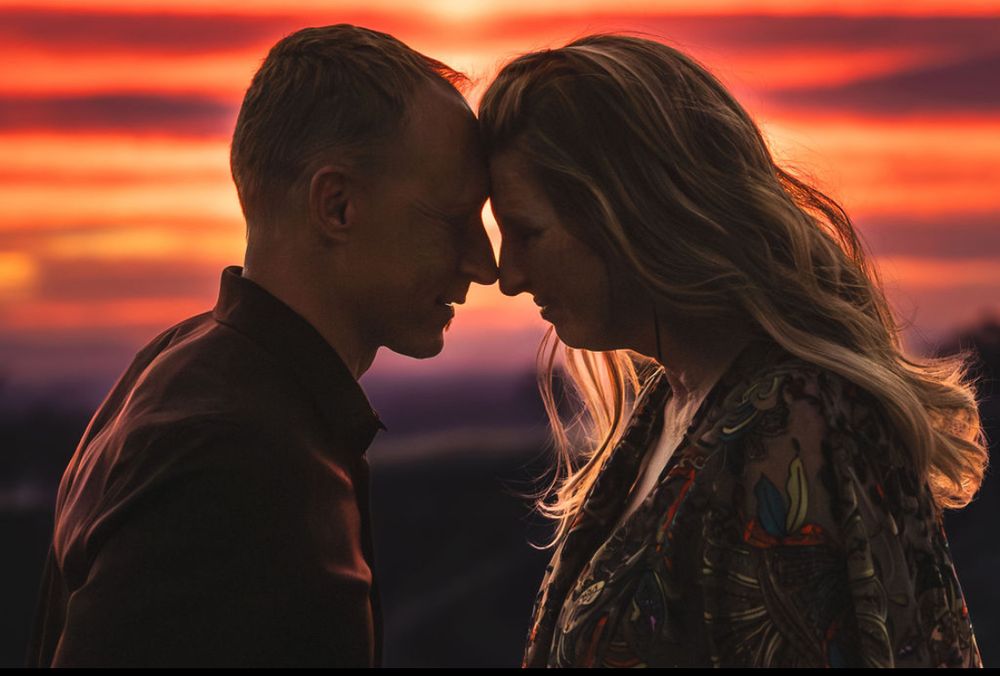 A romantic couple touching foreheads against a stunning red and orange sunset sky backdrop.