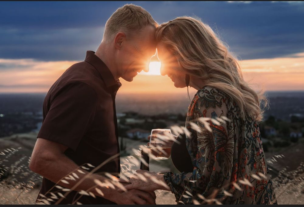 Romantic couple touching foreheads at sunset with city skyline backdrop in golden hour light.