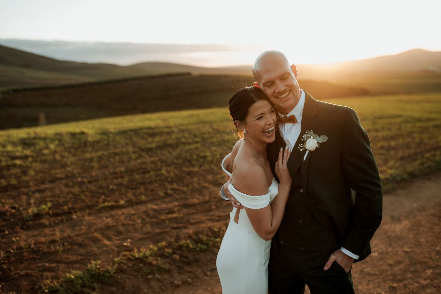Bride in lace gown and groom in tuxedo stand together in a romantic garden archway of lush greenery.