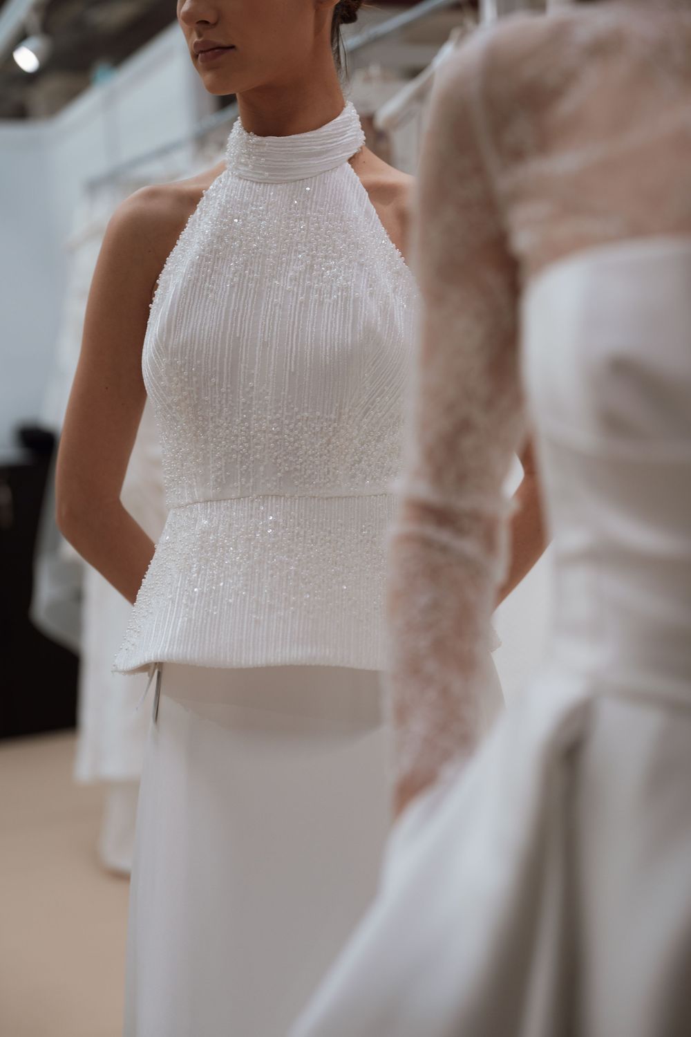 Elegant halter neck bridal gown with pearl embellishments and pleated bodice displayed at a bridal fashion showcase.