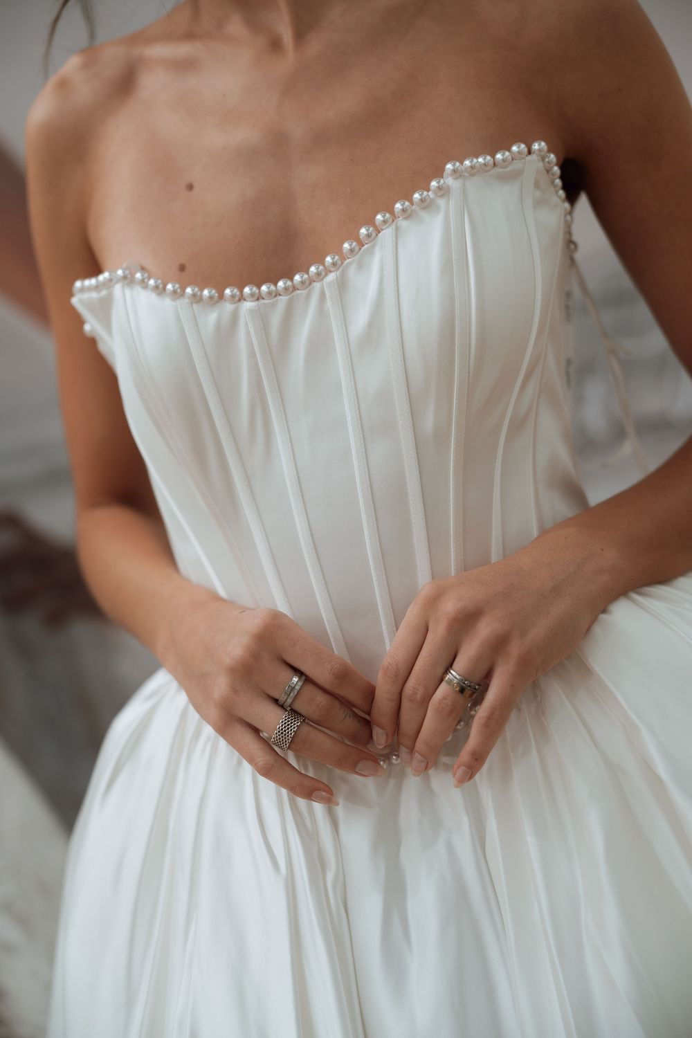 Bride in strapless white wedding gown with pearl neckline detail and corset bodice, wearing silver rings on her hands.