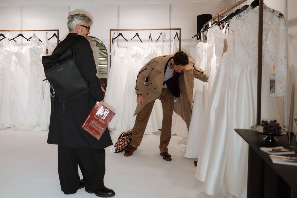 Two people browsing white wedding dresses on racks in a bridal boutique store.