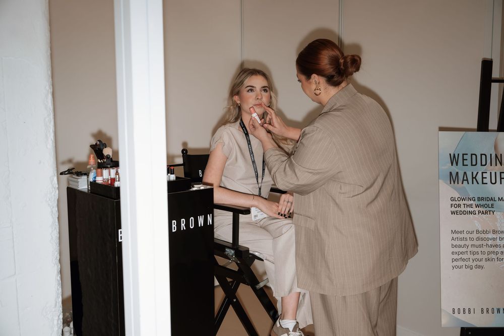 Wedding makeup artist applying makeup to a blonde bride in a bridal suite at a professional makeup station.