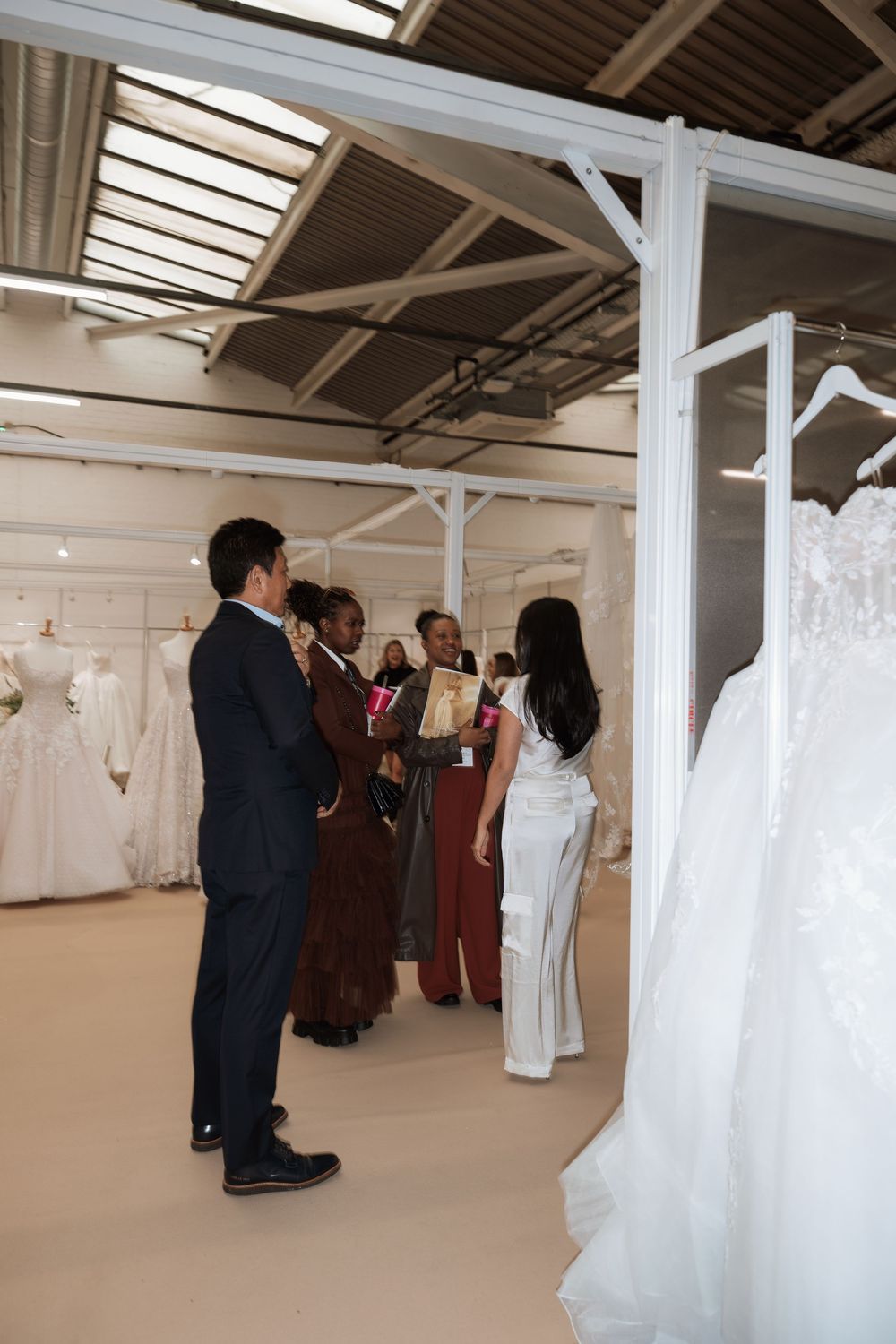 Group of people browsing wedding dresses in a bridal boutique showroom with white gowns on display.