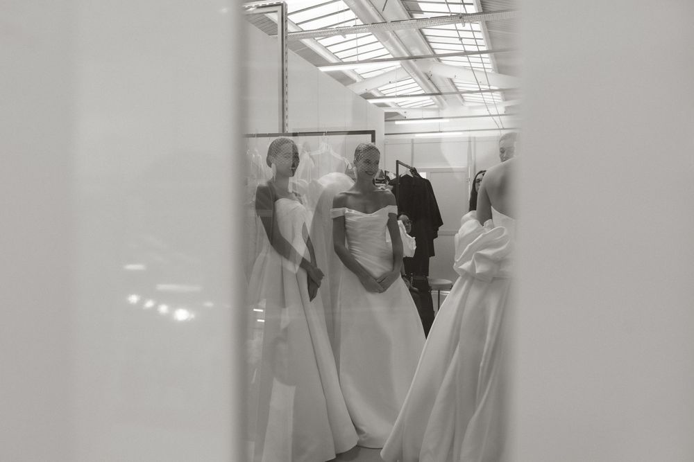 Black and white photo of models wearing elegant white wedding gowns in a bright bridal showroom.