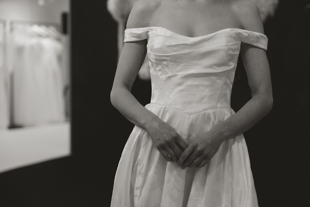 Woman in elegant off-shoulder white bridal gown with clasped hands, captured in black and white photography.