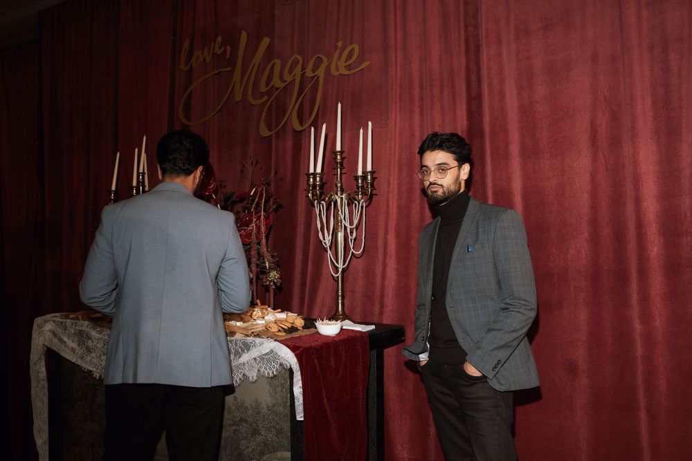 Two men in formal attire stand near an elegant candlelit table at a Jack and Maggie event.