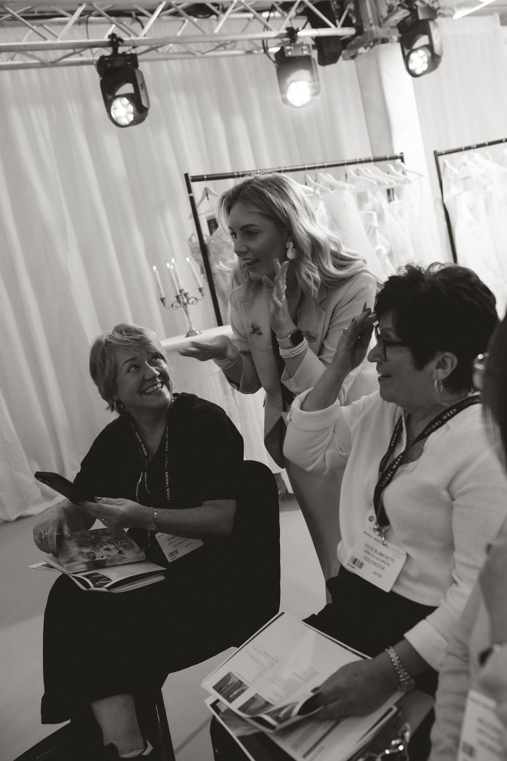 Three women in black and white photo reviewing bridal magazines in a wedding dress boutique showroom.