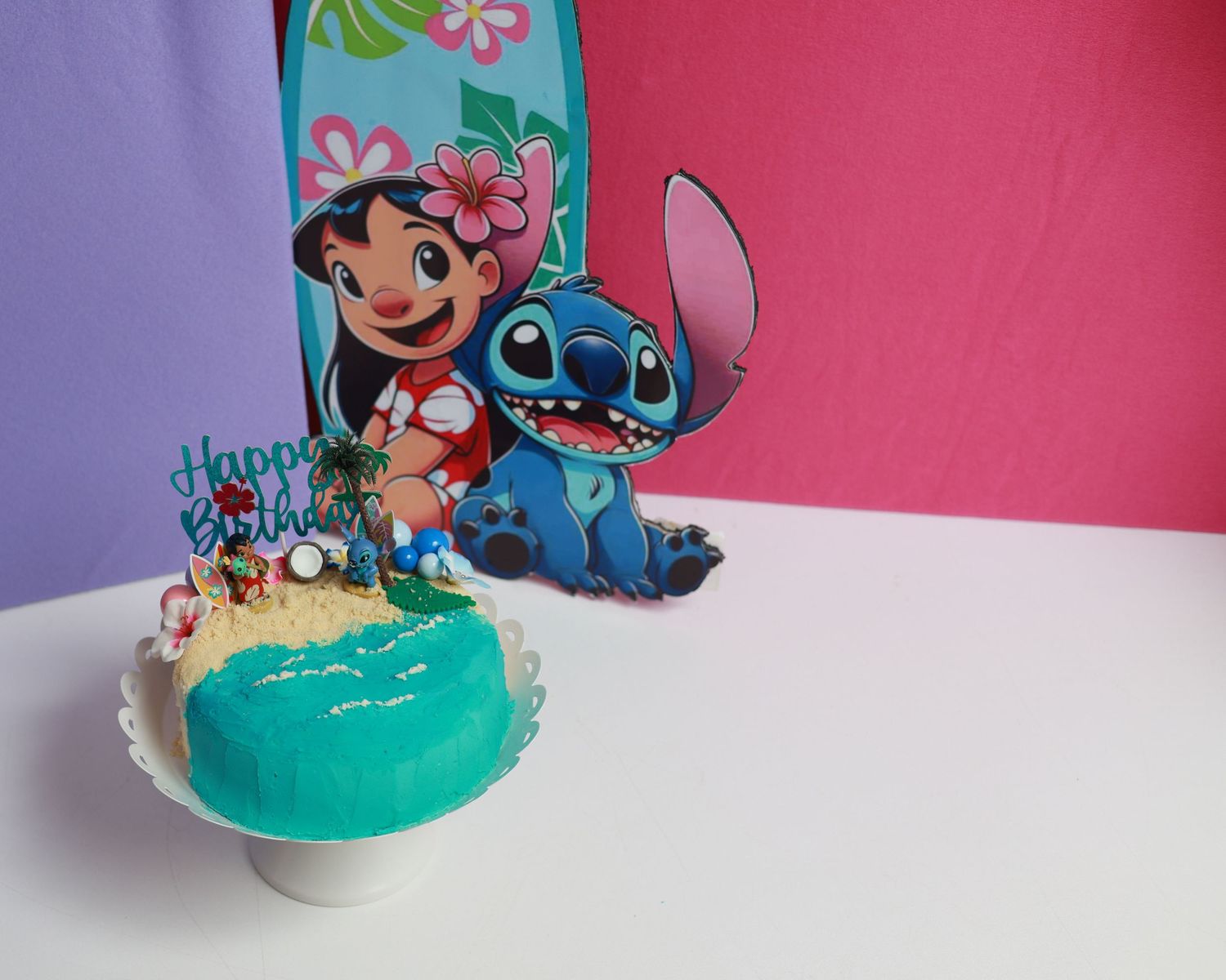 Lilo and Stitch themed birthday cake with turquoise frosting and beach decorations beside Lilo and Stitch character cutouts.