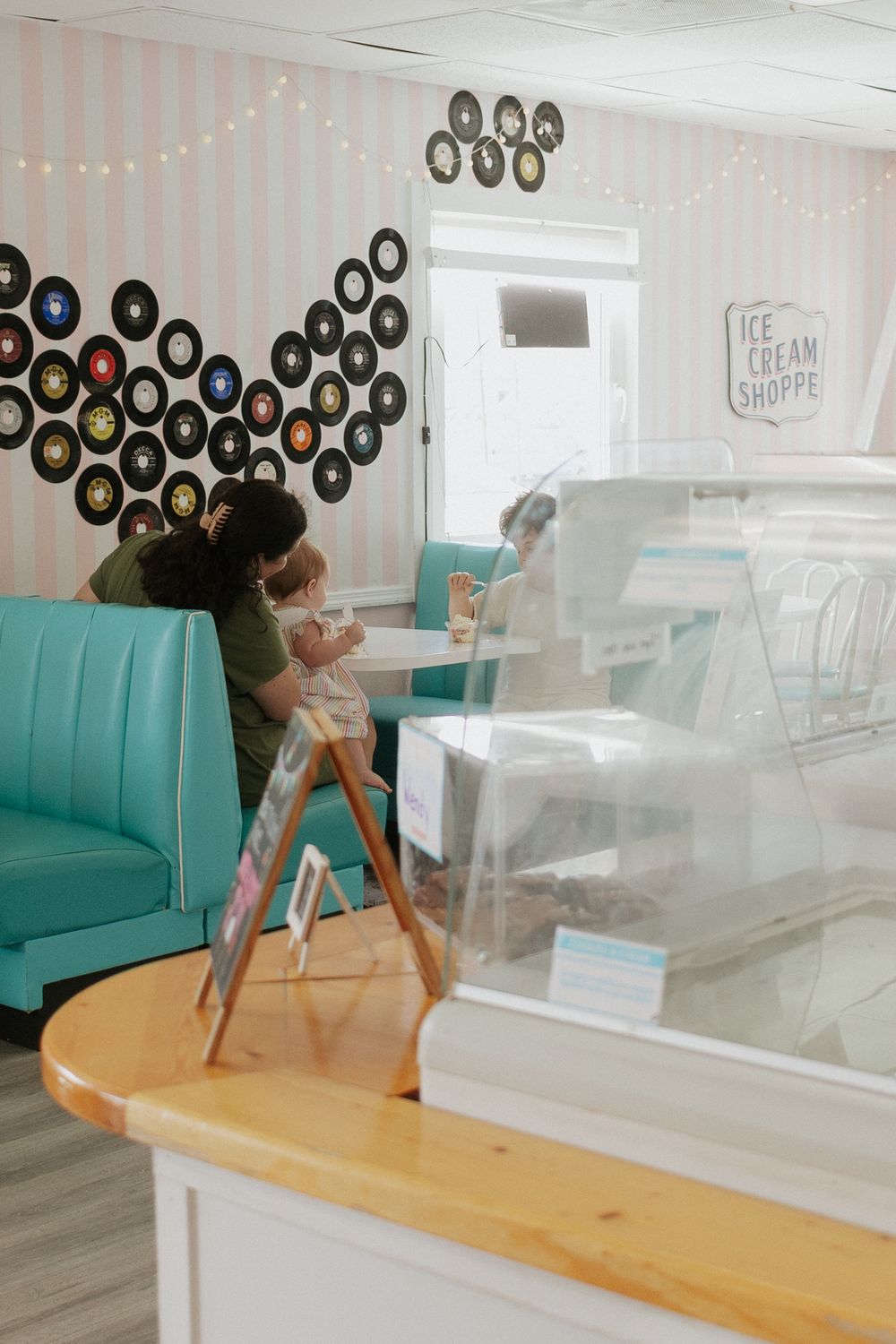 Retro ice cream shoppe with vinyl records wall decor, teal booths, and a glass display counter.
