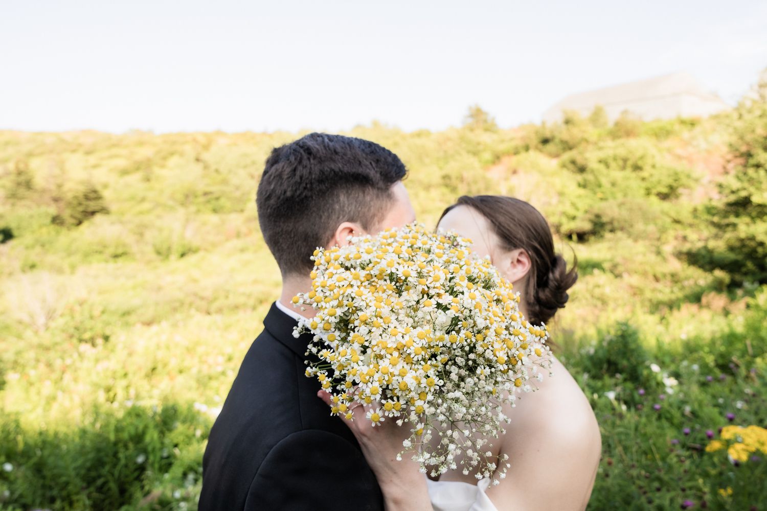 bride and groom kissing pose behind bouquet