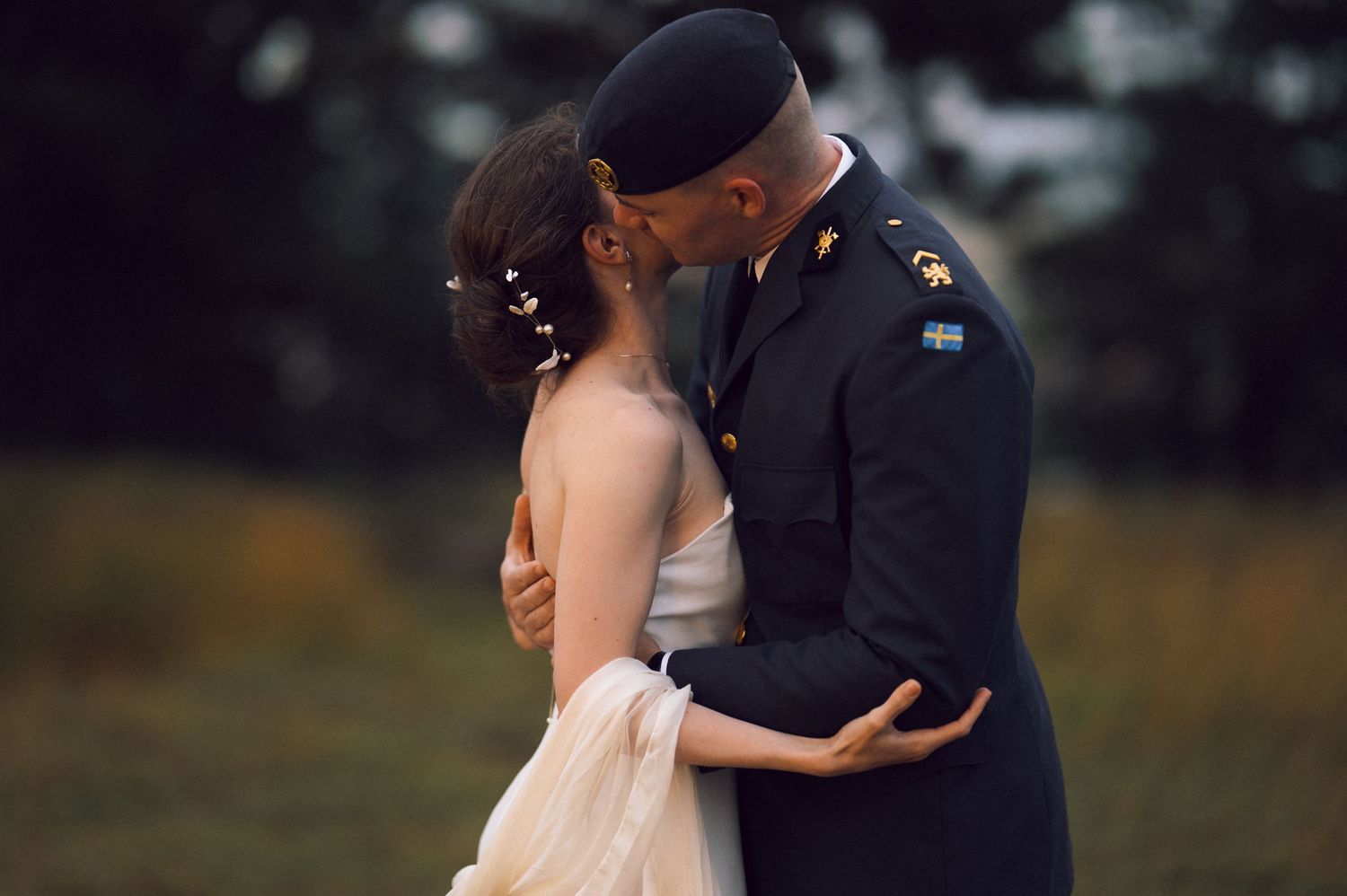 Military groom in dress uniform kissing bride in elegant wedding gown outdoors in a romantic ceremony.