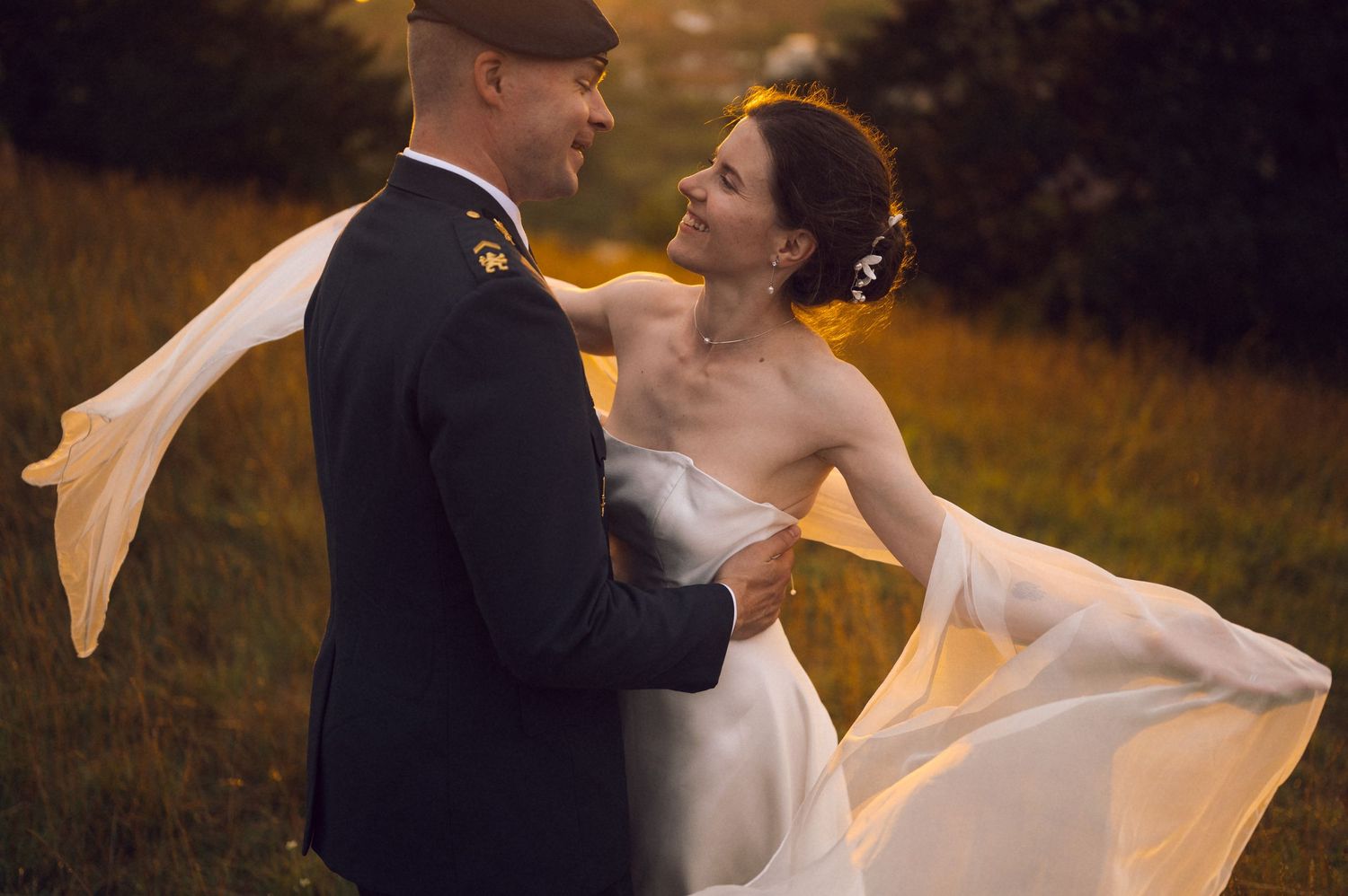 A bride and groom share a romantic dance outdoors at golden hour, her white gown flowing in the breeze.