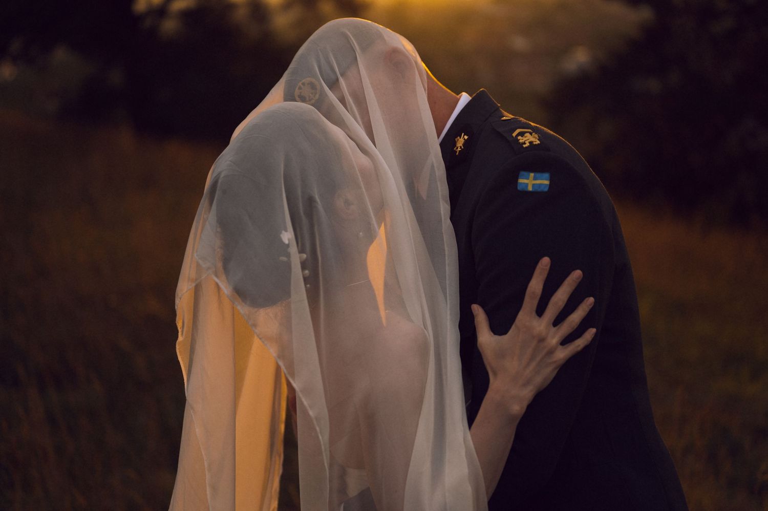 Military groom and bride sharing a kiss under her veil at golden hour sunset in an outdoor wedding ceremony.