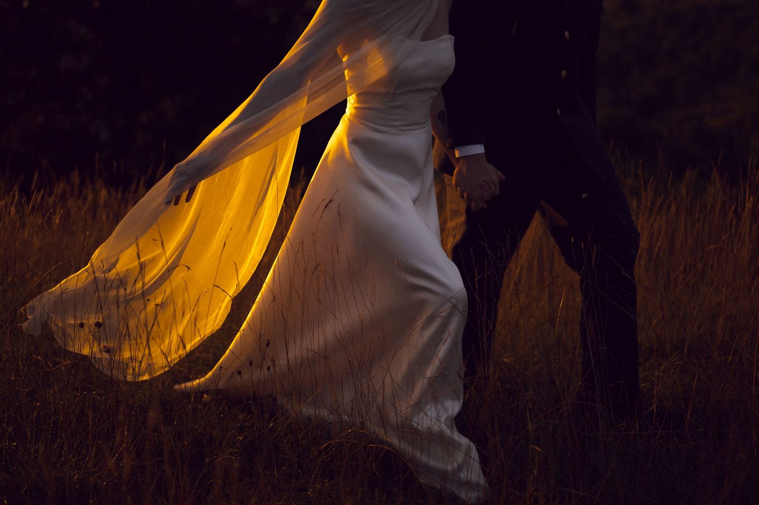 Bride in flowing white wedding dress illuminated by golden light dancing outdoors at night.