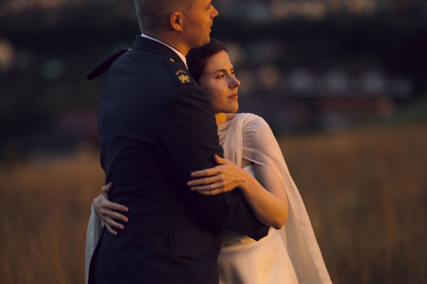 A bride and groom share a tender embrace outdoors at golden hour, with the bride in a white gown and veil.