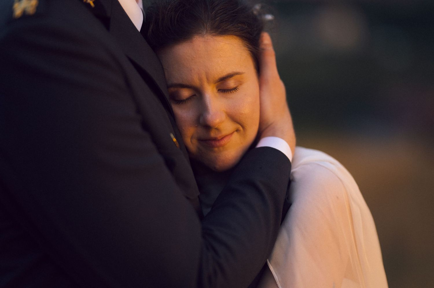 Emotional bride in white veil hugging groom in dark suit, eyes closed, smiling with tears on her wedding day.