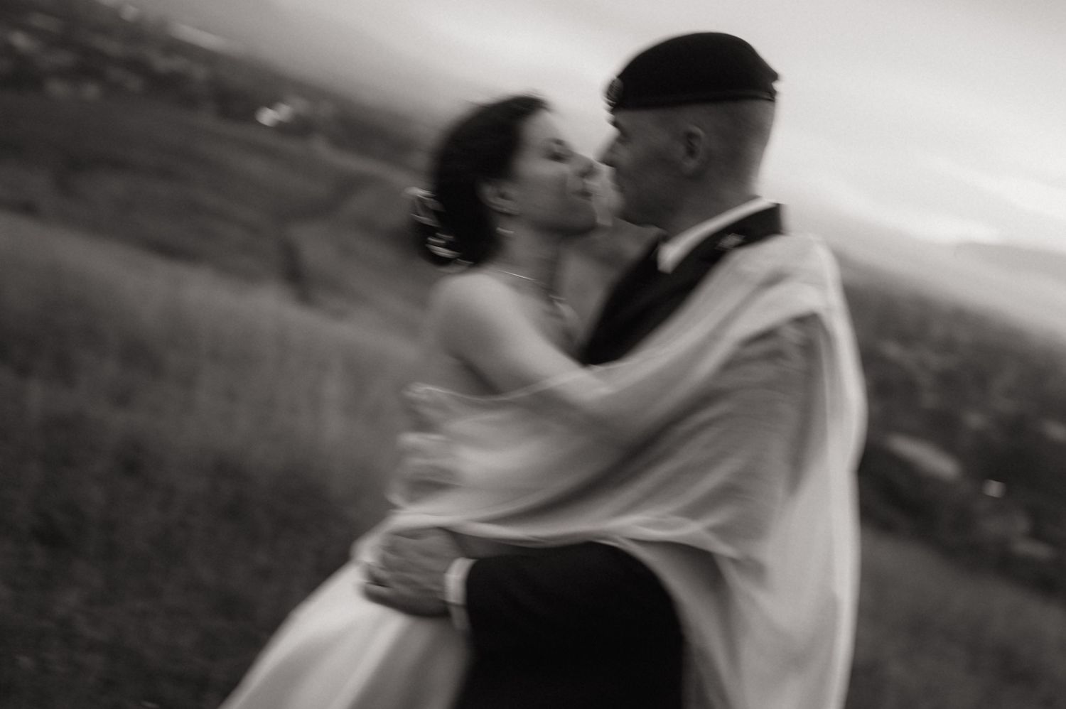 Black and white photo of a couple sharing a romantic kiss outdoors on their wedding day.