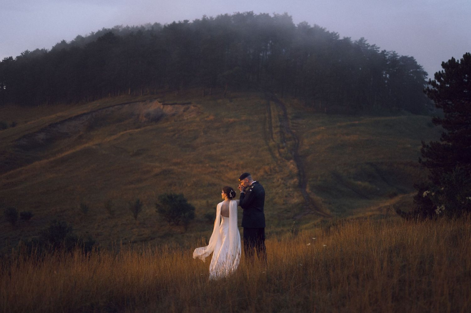 Bride and groom standing in golden meadow with misty green hills backdrop during outdoor wedding photo session.