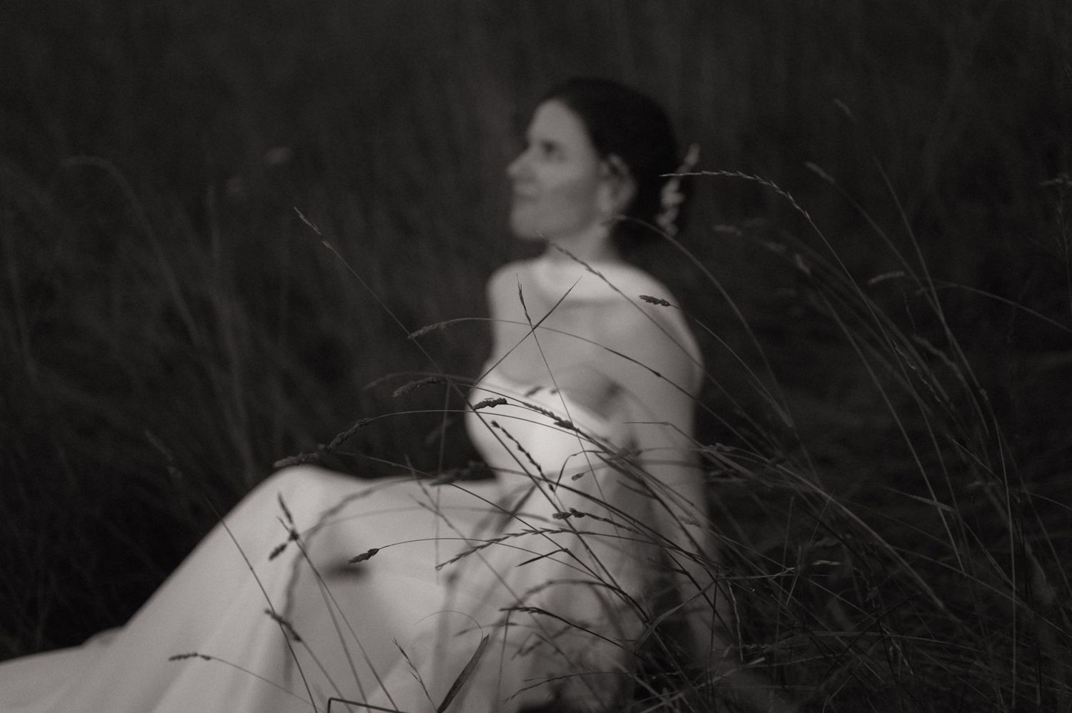 Black and white artistic photo of a woman sitting peacefully among tall wild grass in a serene outdoor setting.