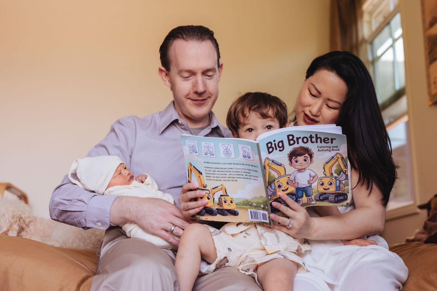 Family reading Big Brother book together, parents sitting with toddler and newborn baby on bed with Santa Barbara newborn photographer.