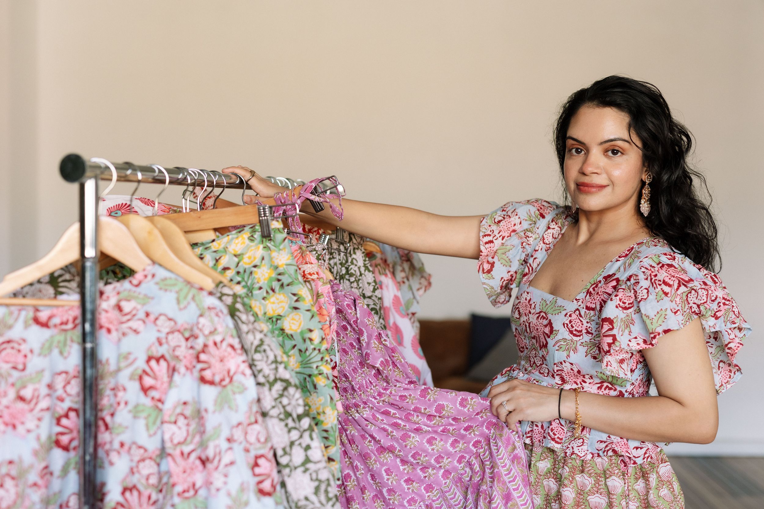 Woman in floral dress arranging colorful floral dresses on a clothing rack in a bright studio.