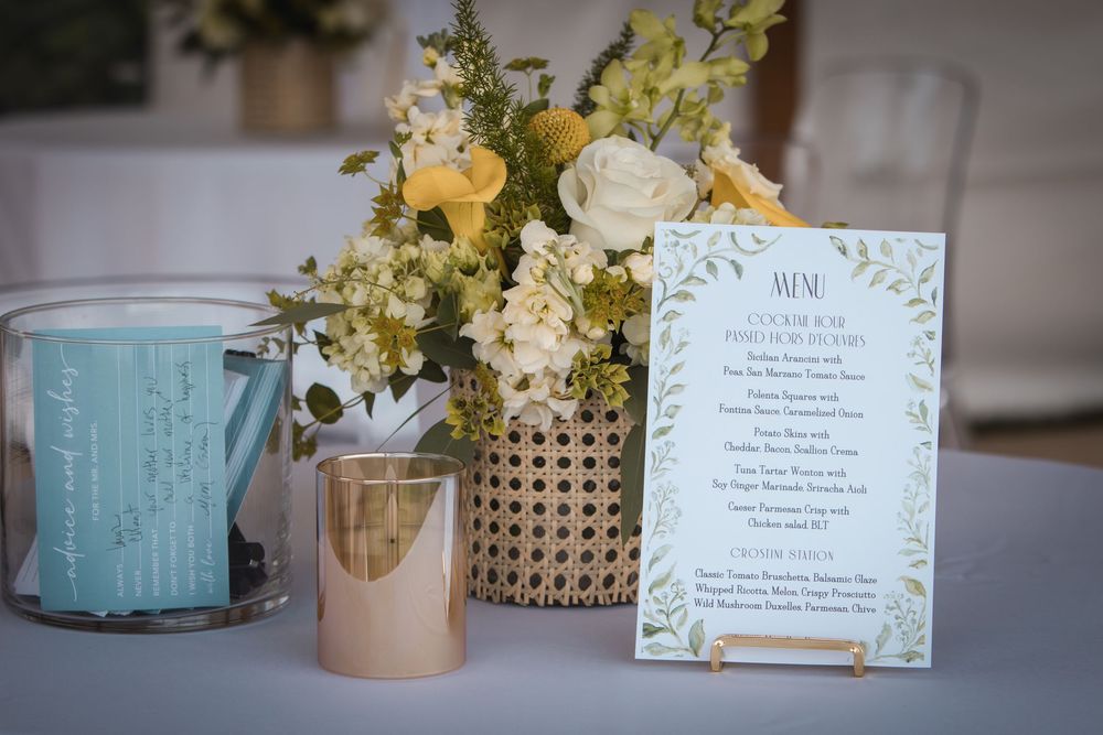 Elegant wedding reception table with floral centerpiece, gold candle, and decorative menu card with greenery border.