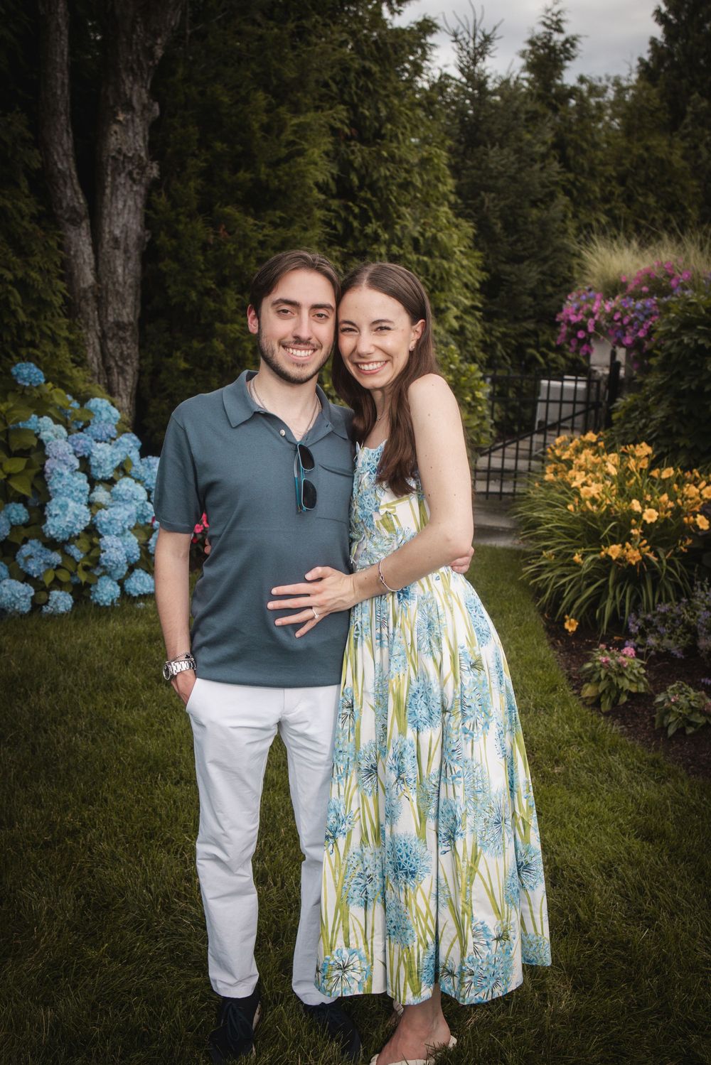 Smiling couple embracing in a lush garden with colorful hydrangeas, wearing casual summer outfits.