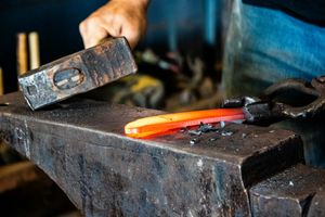 Blacksmith hammering glowing hot orange metal on an anvil in a workshop.