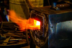 Glowing orange hot metal being heated in a blacksmith forge with bright flames.