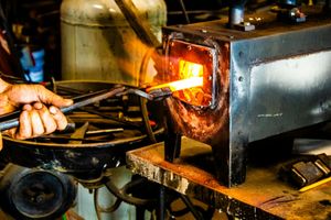 Blacksmith using metal tongs to heat glowing hot iron rod in a forge furnace in a workshop.