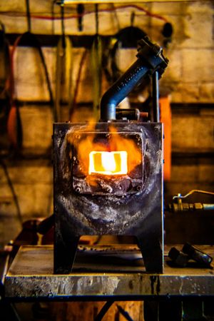 A glowing forge furnace with bright orange flames visible through the door in a rustic blacksmith workshop.
