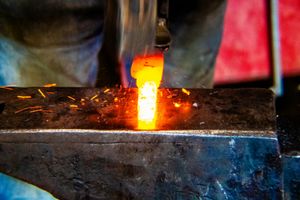 Glowing hot metal being forged on an anvil with sparks flying in a traditional blacksmith workshop.
