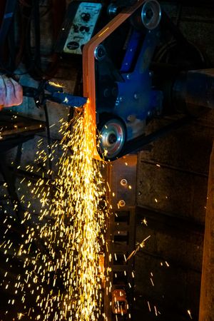 Metal grinder cutting steel with bright orange sparks cascading down in a dark industrial workshop.