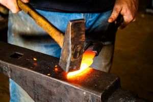 Blacksmith hammering glowing hot metal on an anvil with sparks flying in a traditional forge workshop.