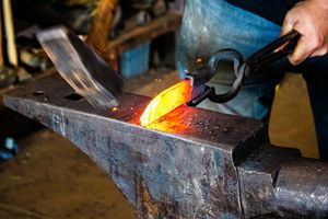 Blacksmith forging glowing hot metal on an anvil using tongs in a traditional forge workshop.
