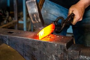 Blacksmith hammering glowing hot metal on an anvil in a forge workshop.