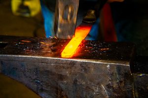Blacksmith hammering glowing red-hot metal on an anvil with sparks flying in a forge.