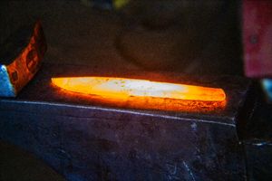 Glowing red-hot metal blade being forged on an anvil in a blacksmith workshop.