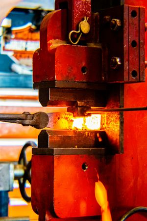 Red industrial forge press shaping glowing hot metal with intense orange heat in a manufacturing workshop.