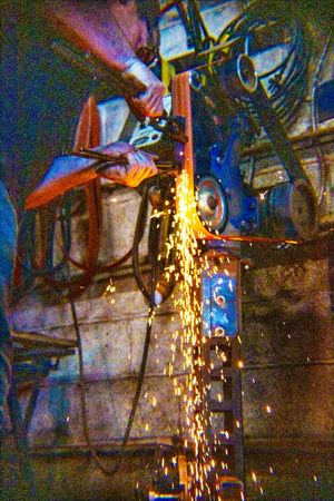 Worker grinding metal with sparks flying in an industrial workshop setting.