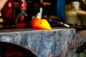 Bright orange-red heated metal piece on a blacksmith anvil ready for forging in a workshop.