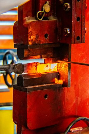 Red industrial hydraulic press forging a glowing hot metal piece in a manufacturing facility.
