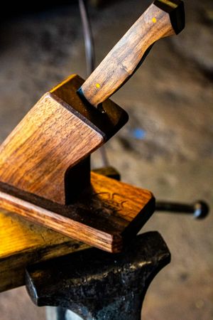 Wooden knife handle clamped in a metal vise on an anvil in a workshop, showcasing handcrafted woodworking craftsmanship.