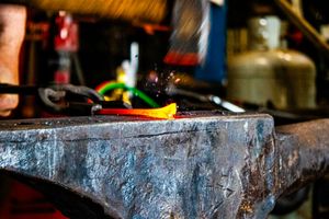 Red-hot glowing metal piece on blacksmith anvil in a forge workshop.