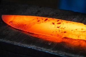 Glowing red-hot knife blade being heat treated in a forge, showing metal hardening process in blacksmithing.
